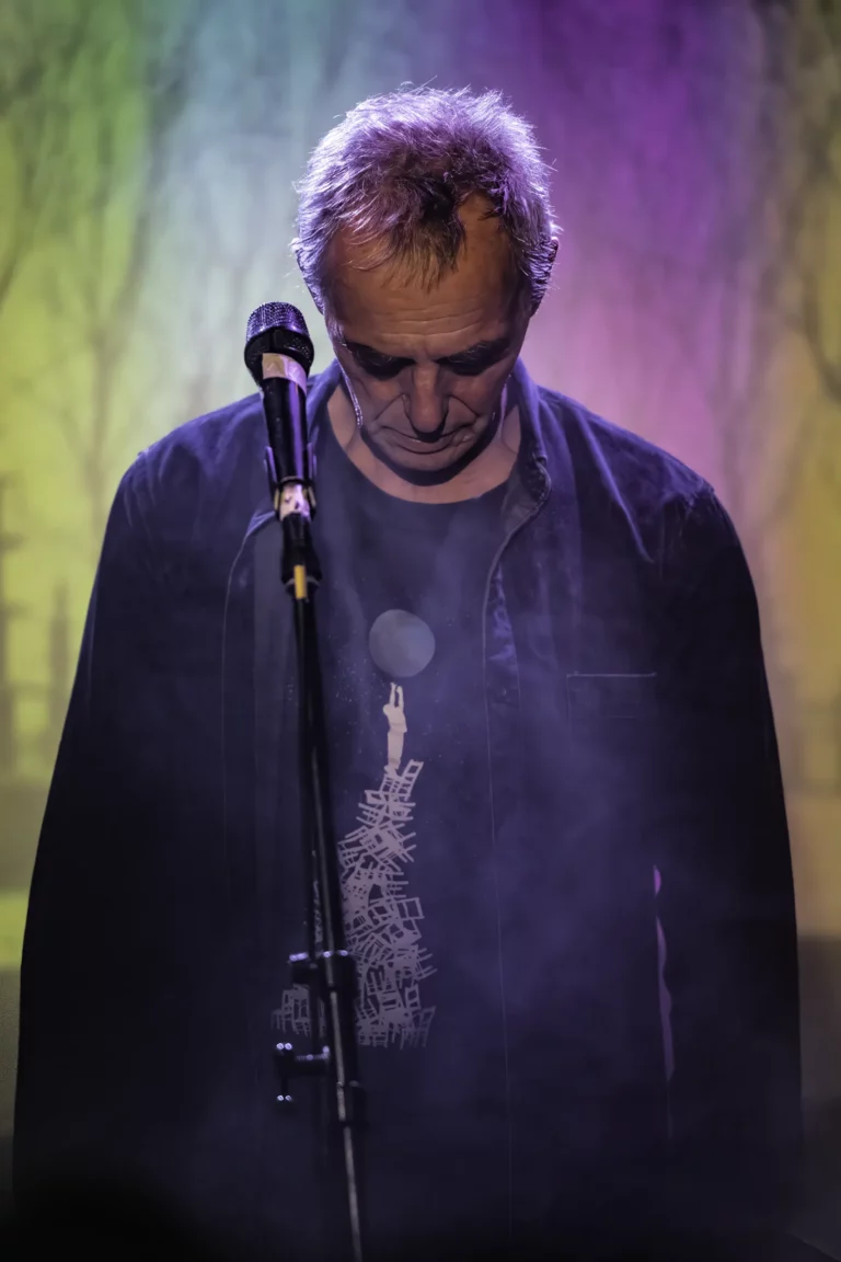 Alain Nitchaeff tête baissée devant le micro, éclairage violet et vert, photo des "36 pagodes postindustrielles" projetée en fond