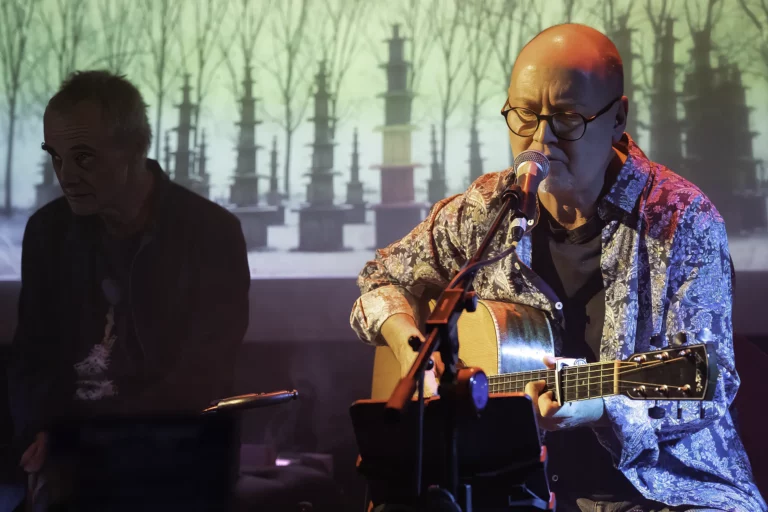Alain Nitchaeff dans l'ombre, Pascal Rinaldi chante à la guitare devant la photo des "36 pagodes postindustrielles" de Julos Beaucarne